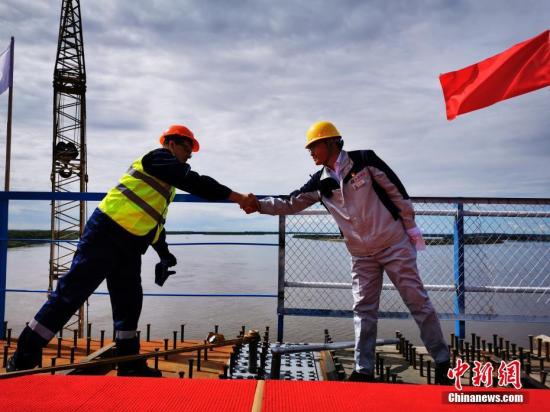 资料图：中俄黑龙江大桥上，双方建设工人安装合龙螺栓并握手祝贺。邵国良 摄